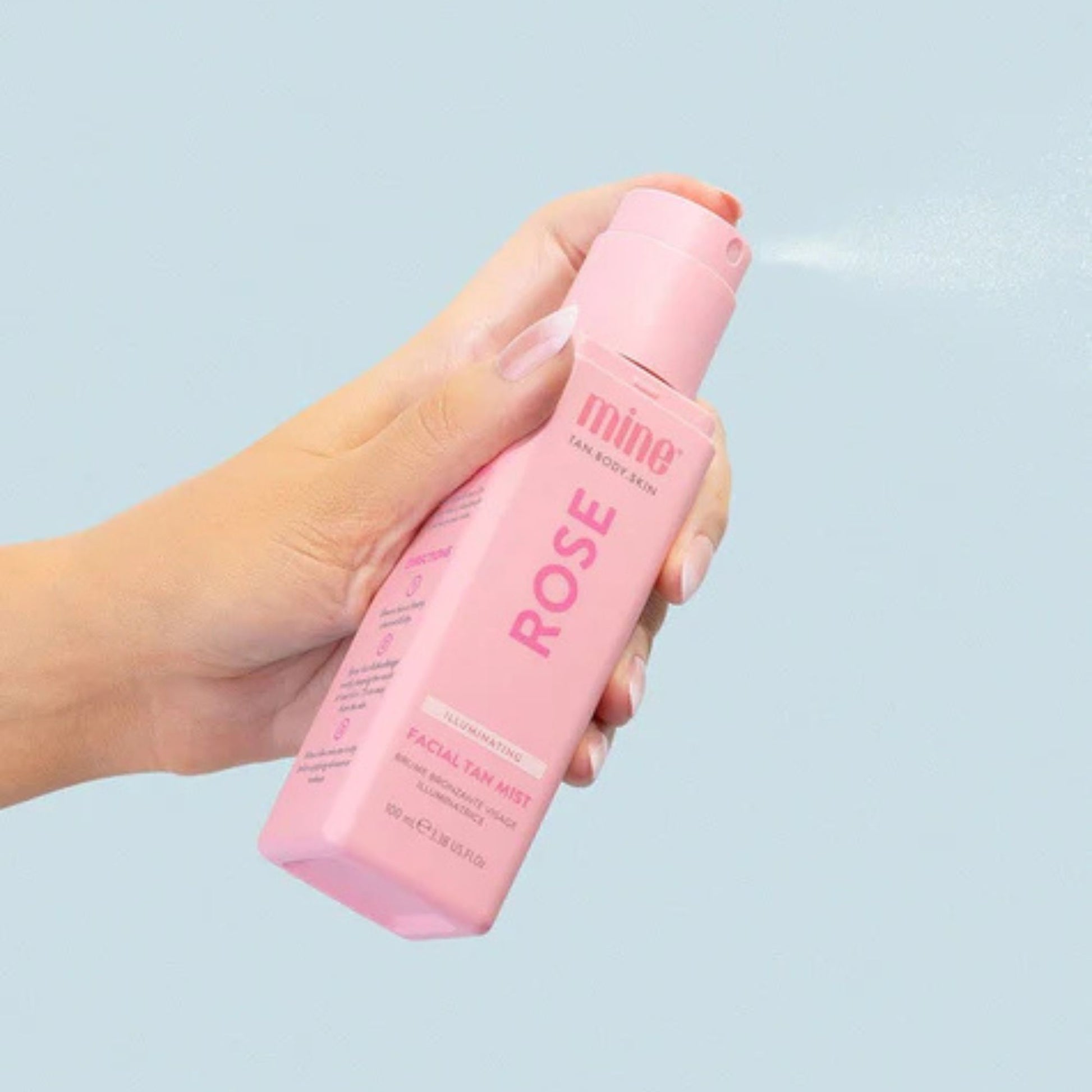 Hand holding a pink bottle of MineTan Rose on a light blue background