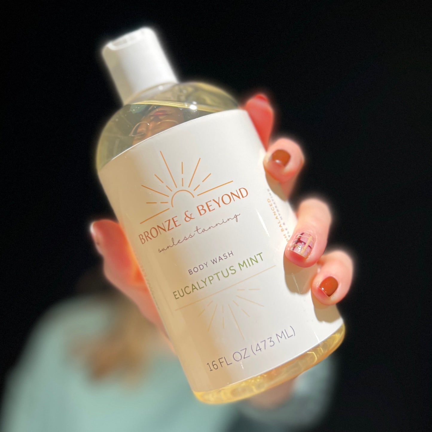 Hand holding a bottle of 'Bronze & Beyond' body wash with a black background